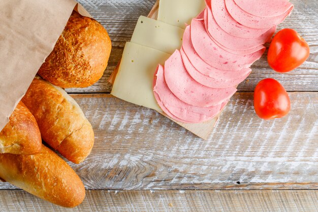 Tomatoes with bread, cheese, sausage on wooden table, flat lay.