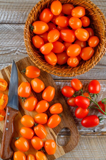 Tomatoes with knife in a basket on wooden and cutting board, top view.