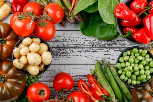 Tomatoes with peppers, potatoes, asparagus, sorrel, green pods, peas, carrots on wooden wall, flat lay.