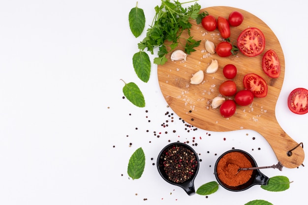 Tomatoes on wooden cutting board with spices top view on white surface