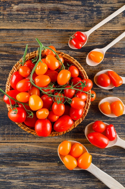 Tomatoes in wooden spoons and basket on a wooden table. top view.