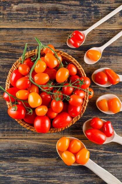 Tomatoes in wooden spoons and basket on a wooden table. top view.