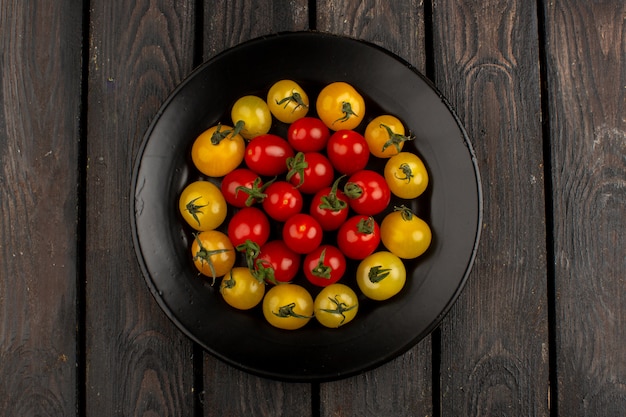 Tomatoes yellow and red round shaped inside black plate on a rustic