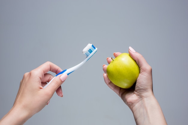 Toothbrush and apple in woman's hands on gray