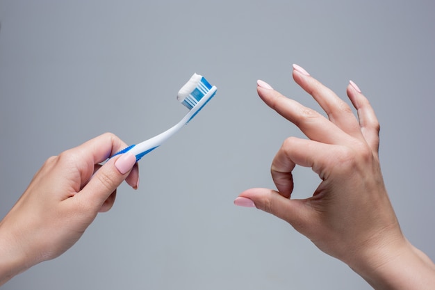 Зубная щетка в руках женщины на сером