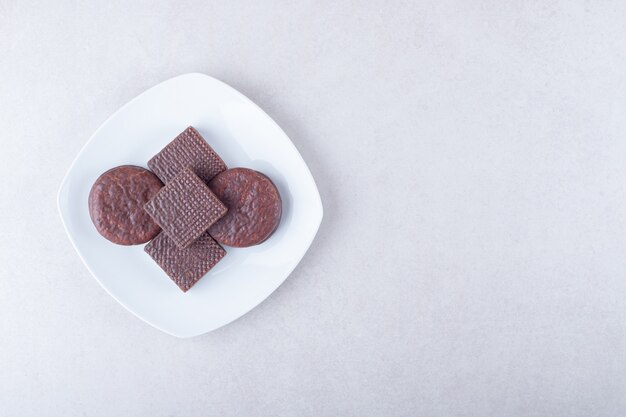 Toothsome chocolate covered cookies and wafer on plate on marble table.