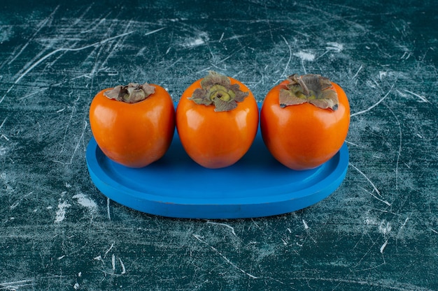 Toothsome persimmon fruit on wooden plate, on the marble background. High quality photo