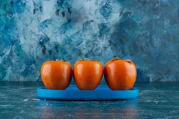 Toothsome persimmon fruit on wooden plate, on the marble table. 