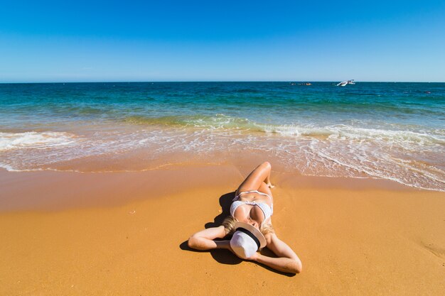 ビーチでリラックスして日光浴をしている水着ビキニの女性のトップ空中ドローンビュー