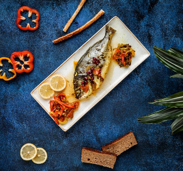 top  baked sea bass serves with vegetables and lemon on platter on blue