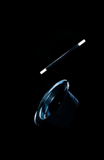 Верхняя черная шляпа и волшебная палочка в воздухе на черном фоне