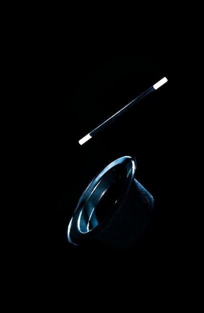 Top black hat and magic wand in air against black background