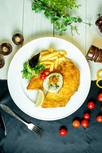 top  breaded chicken fillet served with french fries fried egg and cherry tomatoes on plate