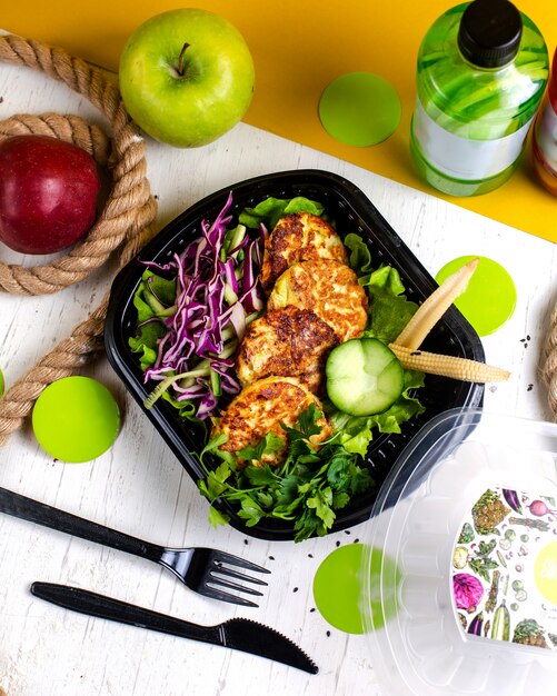 top  broccoli and potato cutlet served with cabbage salad in delivery box on wooden table