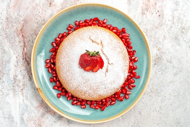 Free photo top close-up view appetizing cake appetizing cake with strawberries and seeds of pomegranates on the blue plate