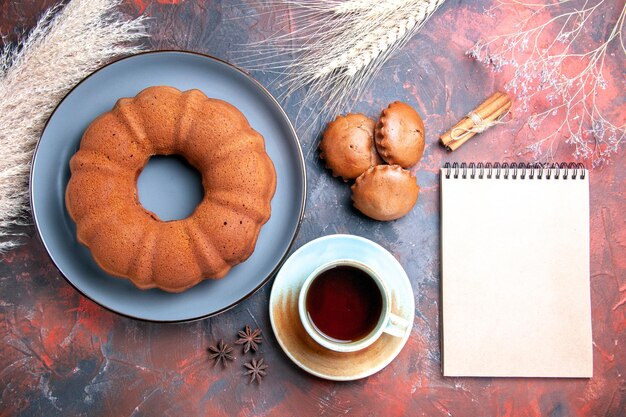 Top close-up view an appetizing cake cake cupcakes a cup of tea cinnamon white notebook wheat ears