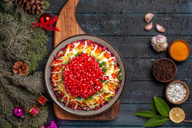 Top close-up view appetizing dish dish on the cutting board next to the bowls of spices branches with cones garlic oil lemon