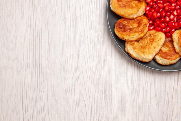 Top close-up view appetizing pancakes black plate of an appetizing pancakes with seeds of pomegranate on the table