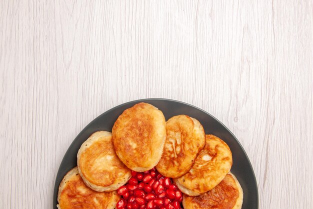 Top close-up view appetizing pancakes plate of an appetizing pancakes with seeds of pomegranate on the white table