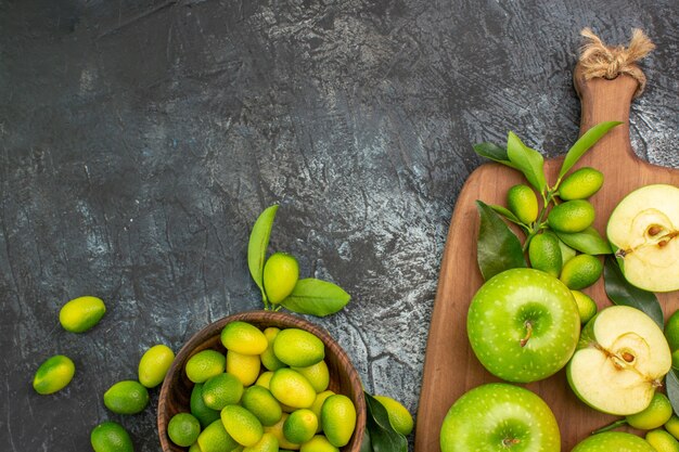 Top close-up view apples bowl of citrus fruits green apples with leaves on the board