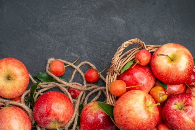 Top close-up view apples rope the appetizing apples cherries in the basket on the dark table