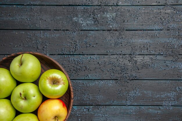 Top close-up view apples on table plate of seven green-yellow-red apples on the left side of dark table