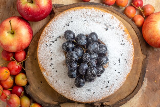 Top close-up view berries apples and berries around a cake with grapes on the wooden board