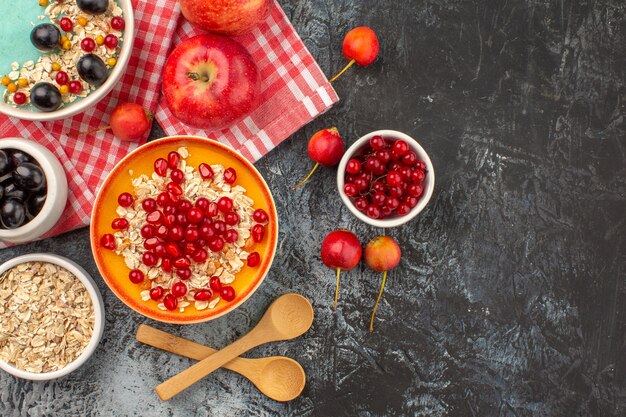 Top close-up view berries bowls of red currants cherries grapes apples pomegranate oatmeal spoons