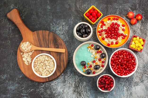 Top close-up view berries grapes cherries red currants pomegranates oatmeal spoon on the board