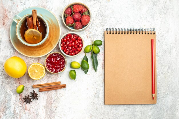Top close-up view berries and tea a cup of tea citrus fruits berries cookies notebook and pencil