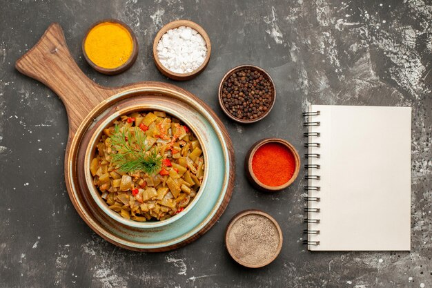 Top close-up view bowl of green beans bowl of beans next to the five kinds of spices and white notebook on the black table