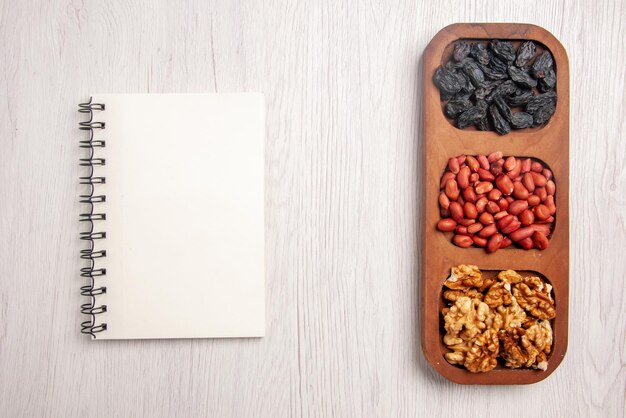 Top close-up view bowls of nuts bowls of different nuts next to the white notebook on the white table