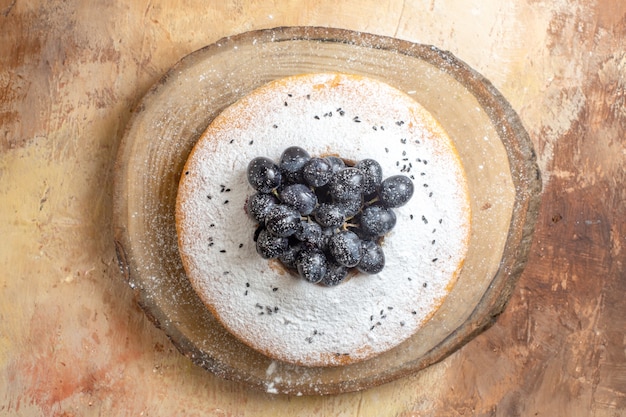 Top close-up view cake an appetizing cake with black grapes on the cutting board