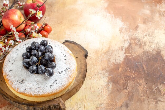 Top close-up view a cake an appetizing cake with grapes on the board cherry apples tree branches