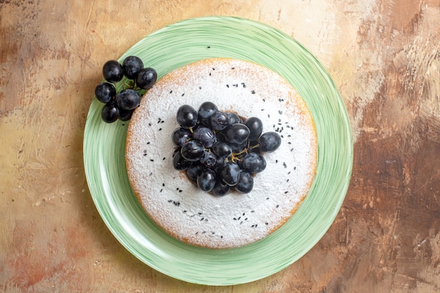 Top close-up view a cake an appetizing cake with grapes and powdered sugar