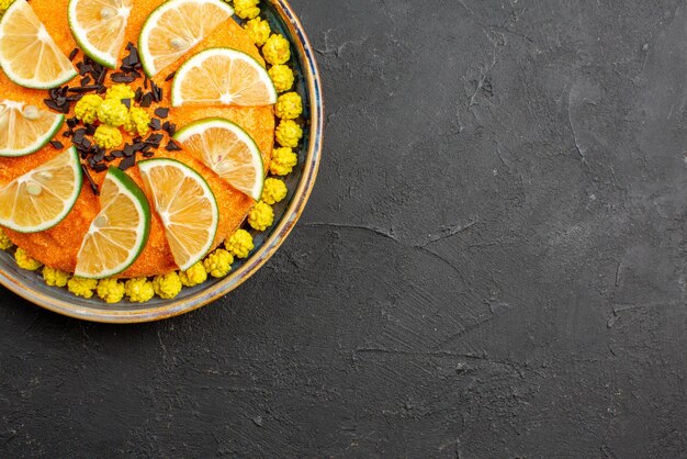 Top close-up view cake appetizing cake with sliced citrus fruit on the left side of the dark table