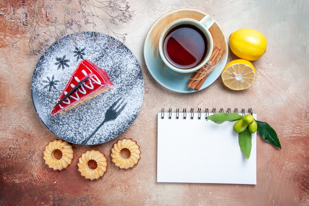 Top close-up view a cake a cake cookies a cup of tea cinnamon lemon white notebook