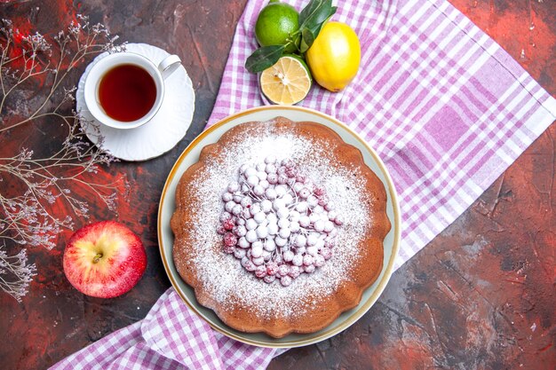 Top close-up view a cake a cake with berries apple a cup of tea citrus fruits on the tablecloth