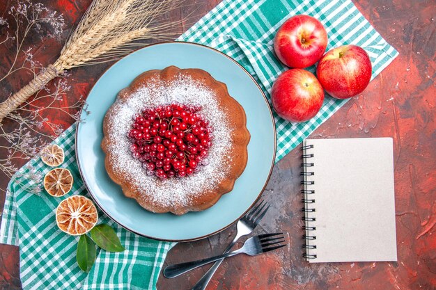 上のクローズアップビューケーキテーブルクロスフォークノートに赤スグリリンゴレモンとケーキ