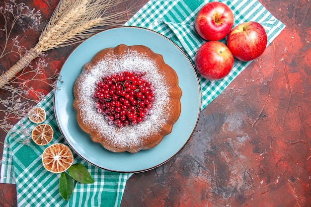 Top close-up view a cake a cake with red currants lemon with leaves apples on the tablecloth