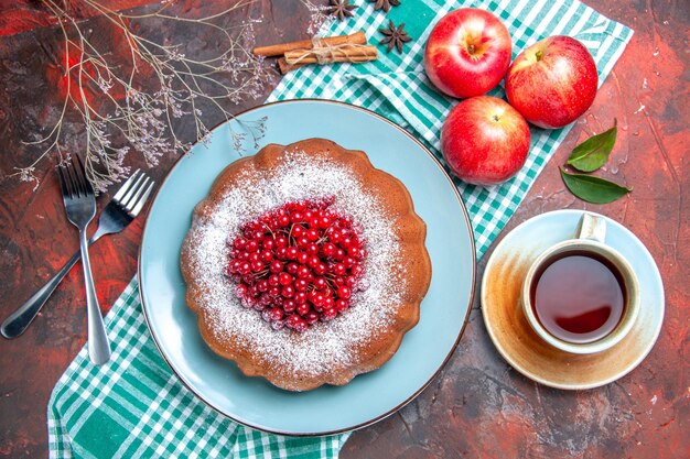 Top close-up view a cake a cake with red currants three apples a cup of tea forks cinnamon