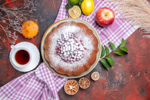 Top close-up view a cake a cup of tea a cake apple lemons with leaves on the tablecloth cupcake