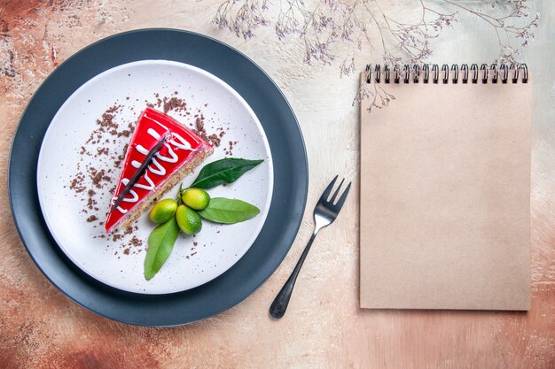 Top close-up view a cake plate of cake with chocolate sauces citrus fruits fork cream notebook