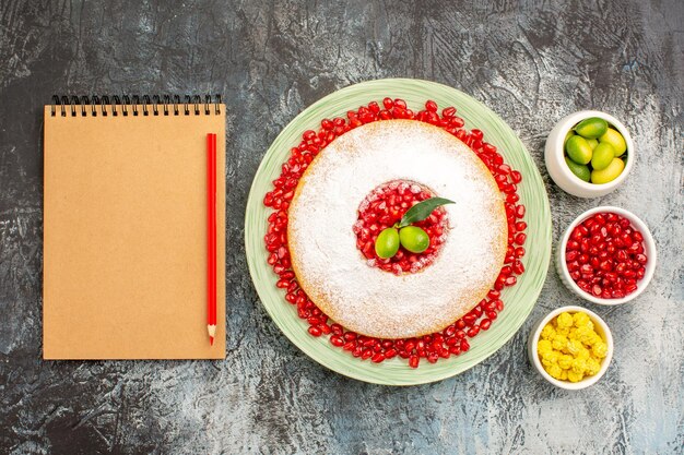 Top close-up view cake and sweets an appetizing cake citrus fruits candies notebook red pencil