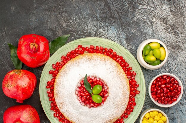 Torta vista ravvicinata dall'alto con melograno tre ciotole di melograno di frutti di bosco e un piatto di torta