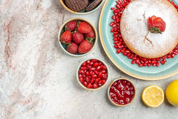 Top close-up view cakes appetizing cake of strawberries and pomegranate lemon bowls of berries cookies on the table