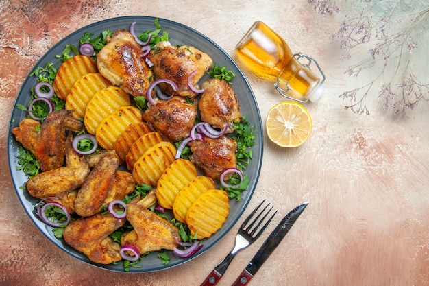 Top close-up view chicken the appetizing chicken wings potatoes herbs onions oil lemon fork knife