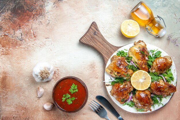 Top close-up view chicken board with chicken with herbs garlic oil fork knife lemon sauce