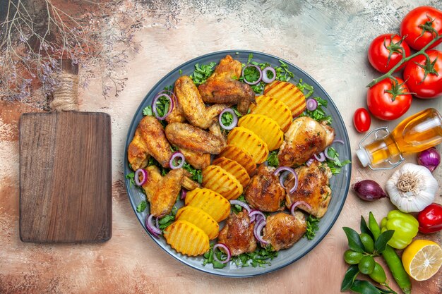 Top close-up view chicken chicken wings potatoes onion herbs vegetables the cutting board