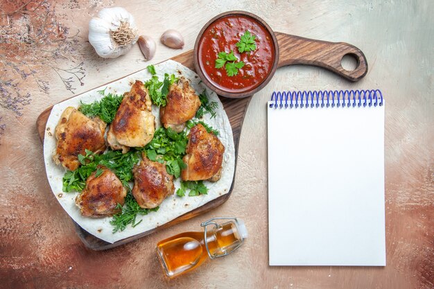 Top close-up view chicken chicken with herbs bowl of sauce bottle of oil garlic white notebook